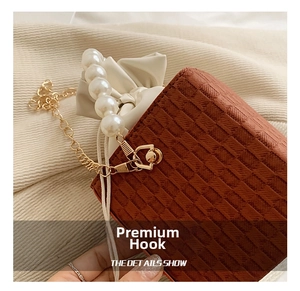 Macro detail of golden metal hook connection on brown textured leather crossbody bag
