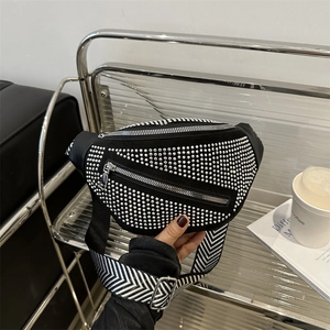 Black punk crossbody bag with silver studs and wide striped shoulder strap on a chair