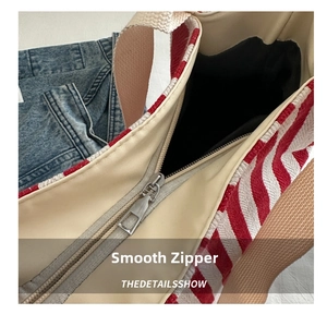 Detailed close-up of the smooth silver zipper closure on a red striped canvas tote bag