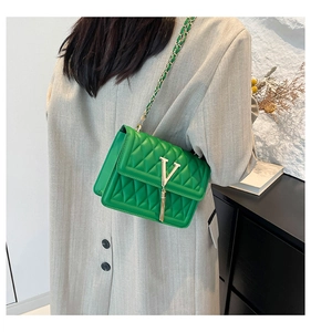 Close-up of green quilted crossbody bag with gold V-logo and chain strap on a model