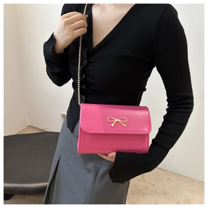 Detail of rose red shoulder bag with golden bow hardware and elegant chain strap
