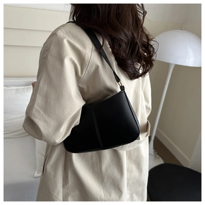 Minimalist black hobo shoulder bag with matte finish worn by a model in a beige trench coat