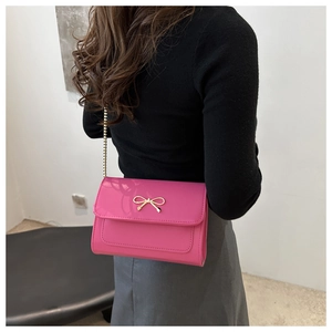 Detail of pink glossy patent leather bag with gold bow clasp and metal chain strap