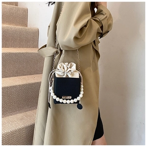 Dettaglio borsa nera effetto coccodrillo con manico di perle e catena d'oro su un trench beige
