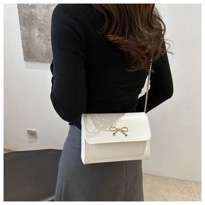 Close-up of white crossbody bag with gold bow clasp and metallic chain on a model