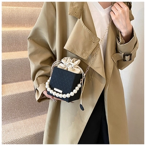 Detail of black woven bucket bag featuring large pearl handle and cream drawstring closure