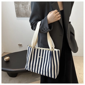 Detail of blue and white striped canvas tote bag with white woven handle and metal plaque