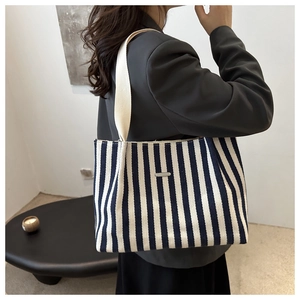 Blue and white striped canvas tote bag with metal logo shown on a person's shoulder