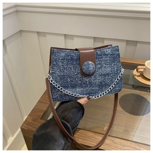 Detail of the blue denim tote bag featuring brown leather trim and a silver metal chain