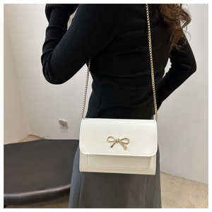 Close-up of white crossbody bag featuring a golden bow buckle and fine metal chain strap