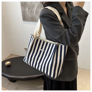 Detail of blue and white striped canvas tote bag with metal plaque and beige straps