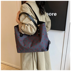Grey fabric tote bag with red polka dots and black straps shown on a model side view