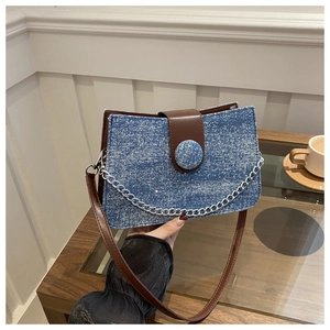 Macro view of blue denim tote with brown leather strap and silver chain detail