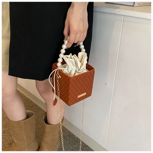 Détail du sac seau marron tressé avec poignée en perles et bandoulière dorée