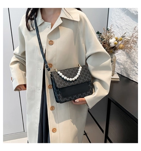 Close-up of black crossbody bag featuring pearl chain strap and letter M monogram pattern