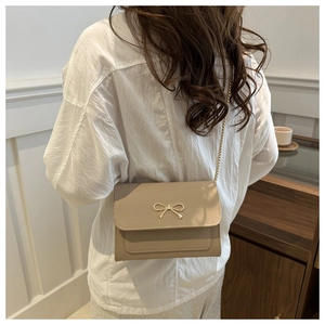 Elegant beige flap crossbody bag with gold bow ornament and chain strap for women