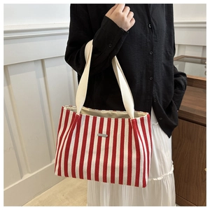Close-up of a red and white striped canvas tote bag with metal nameplate and cotton straps