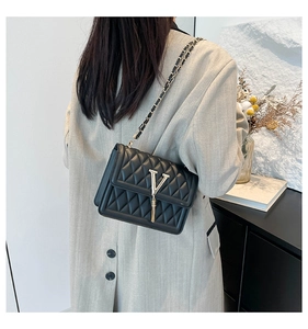 Detail of a black quilted crossbody bag with a gold V logo and tassel on a model