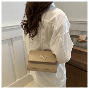 Close-up of beige crossbody bag featuring a golden bow metal clasp and chain strap