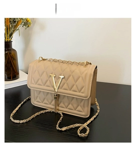 Detail of khaki quilted shoulder bag with golden V-clasp and fringe pendant detail
