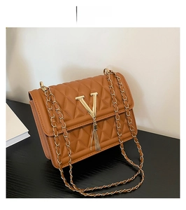 Detail of brown quilted leather bag with gold V-logo, tassel and metal chain strap