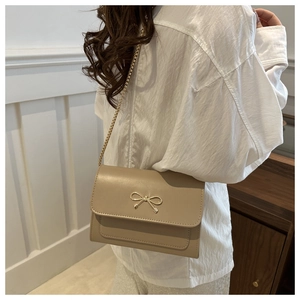 Close-up of beige crossbody bag with gold bow clasp and elegant chain strap details