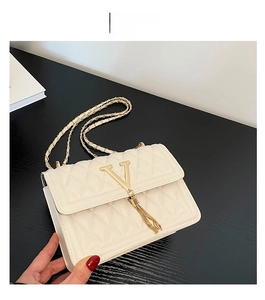 Detail of white quilted crossbody bag with golden V-logo, tassel, and chain strap
