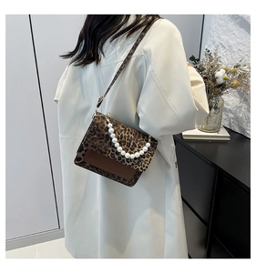 Detail of leopard print crossbody bag with pearl handle worn with a beige trench coat