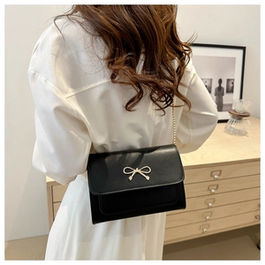 Detailed side view of black crossbody bag with golden bow buckle and chain strap