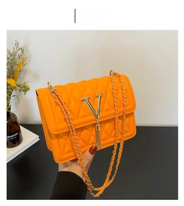 Detail of quilted orange chain bag featuring a gold V-shaped buckle and metal tassel