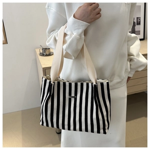 Detail of black and white striped canvas tote bag with woven straps and metal logo plate
