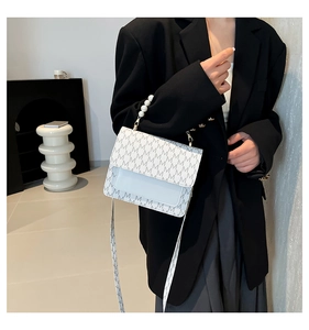 Detail of trendy small square bag with pearl handle and monogram print on white leather