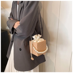 Detail of a beige cube bag featuring large pearl handle and woven texture in use
