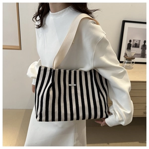 Close-up of black and white striped tote bag with wide strap and metallic logo plate