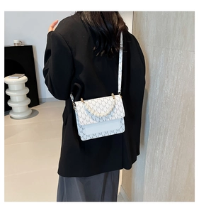 Detail of crossbody bag with M-letter print and pearl handle shown on a model outfit