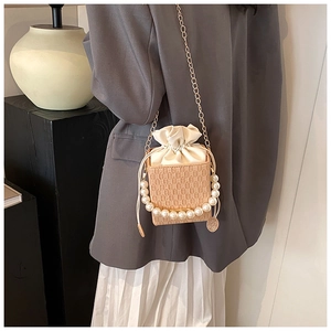 Detail of a chic beige woven mini bag featuring large pearls and a gold chain strap