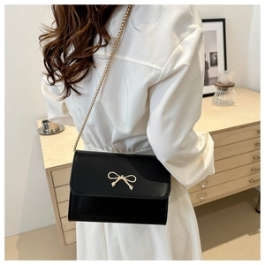 Woman wearing stylish black faux leather shoulder bag with golden bow clasp and chain strap