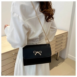 Close-up of black crossbody bag with gold bow clasp and chain strap on a model