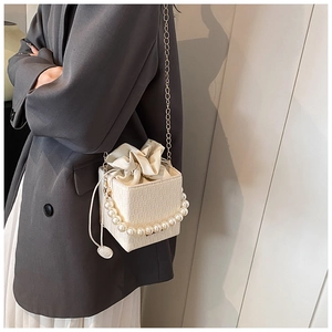 Detail of white crocodile pattern square bag with pearl handle and gold chain strap
