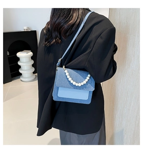 Detail of denim crossbody bag with white pearl handle worn over a black blazer