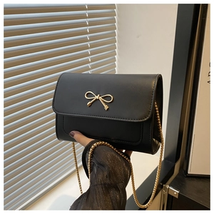 Close-up of black leather crossbody bag featuring a golden bow buckle and fine metal chain