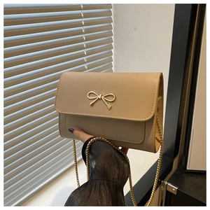 Close-up of beige shoulder bag featuring a gold bow buckle and delicate chain strap