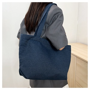 Detail of a large dark blue denim tote bag showing thick texture and wide shoulder strap