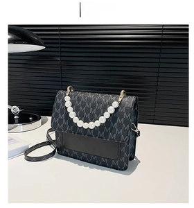 Detail of black crossbody bag with grey letter prints and white pearl handle ornament