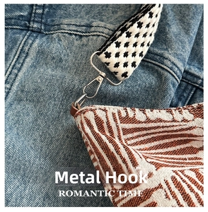 Detail of silver metal hook and checkered strap on a striped canvas shoulder bag
