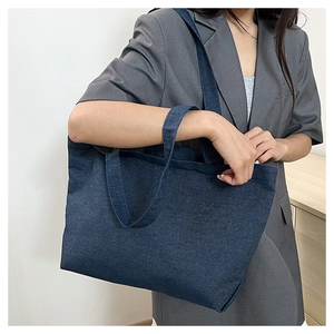 Detail view of large navy blue denim tote bag worn by a model for a stylish casual look