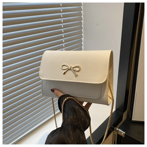 Detail of a creamy white crossbody bag with a golden bow buckle and chain strap