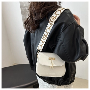 Detail of white square bag featuring gold hardware and a cute deer charm on wide strap