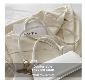 Detail of white minimalist crossbody bag showing a unique knotted handle and gold hardware