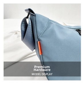 Detail of blue nylon crossbody bag featuring black metal zipper and orange side label